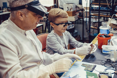 Male teacher teaching small boy how to repair computer part in laboratory.