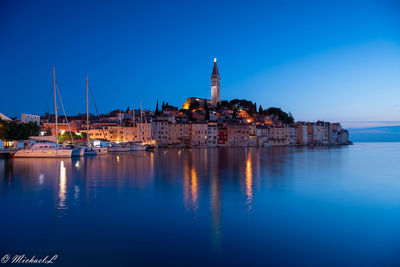 Illuminated buildings by sea against clear blue sky