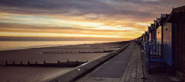 Row of huts at beach against sky during sunset