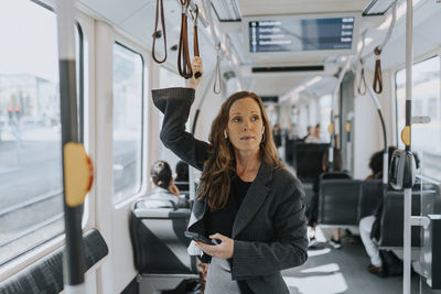 Female passenger holding smart phone while standing in train