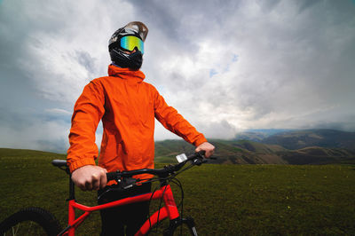Portrait of a male cyclist in an orange windbreaker and full face helmet with goggles against the