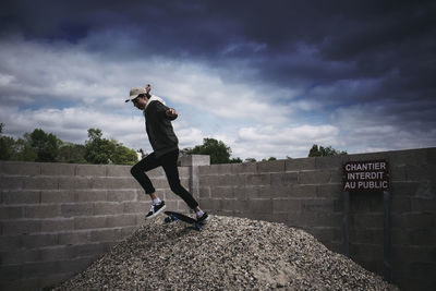 Full length of man skateboarding against cloudy sky