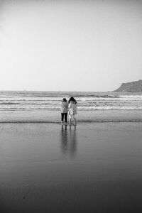 Rear view of woman walking at beach against clear sky