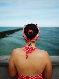 Rear view of mid adult woman looking at sea while standing by railing against cloudy sky