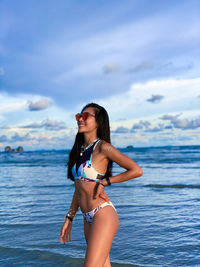 Young woman in bikini standing by sea against sky