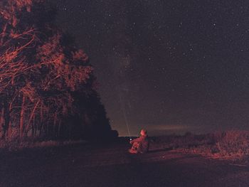 Man sitting on field against sky at night