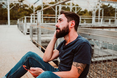 Young man looking away while sitting outdoors