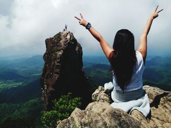 Rear view of woman showing peace sign on cliff
