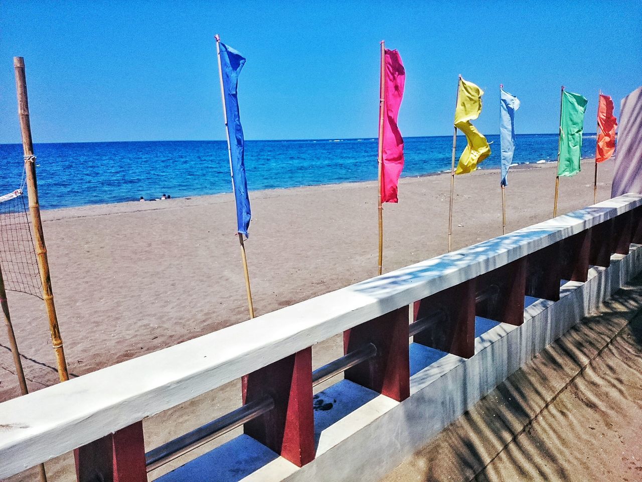 sea, horizon over water, water, blue, beach, in a row, sky, railing, tranquility, shore, day, nature, tranquil scene, built structure, outdoors, no people, sand, beauty in nature, sunlight, multi colored