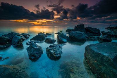 Rocks at sea shore against sky during sunset