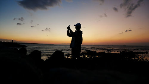 Silhouette man photographing sea against sky during sunset