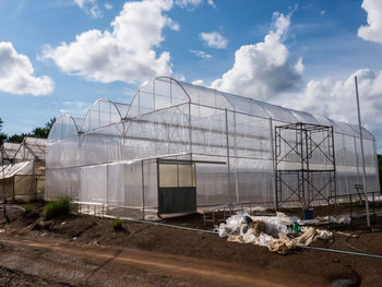 View of greenhouse on field against cloudy sky