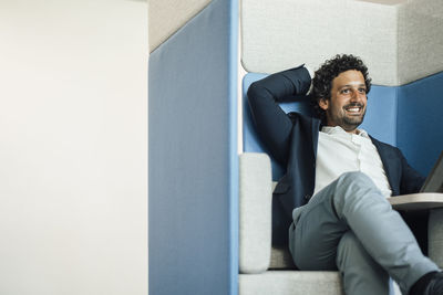 Happy businessman with legs crossed at knee in office