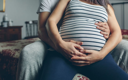 Midsection of couple sitting on bed at home