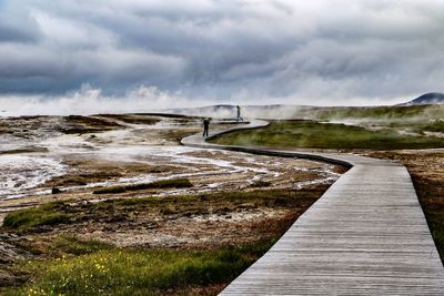 View of footpath leading towards water against sky