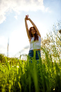 Full length of young woman standing on grassy field against sky