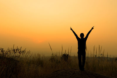 Silhouette person standing on grass at sunset