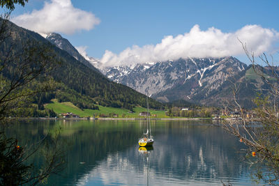 Scenic view of lake, sailboat and snowcapped mountains against dramatic sky