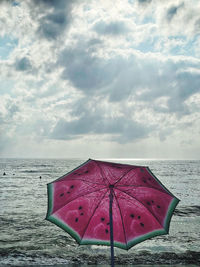 Pink umbrella on beach against sky