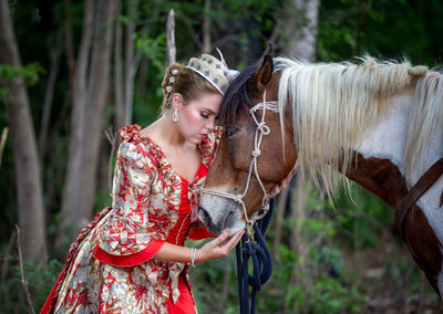 Woman in traditional clothing standing by horse against tree