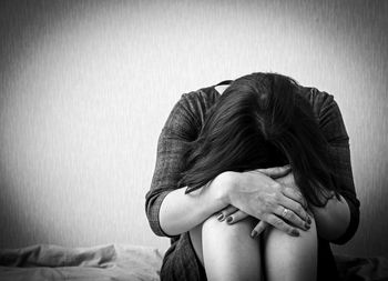 Depressed mature woman sitting on bed by wall