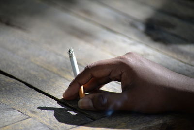 Cropped image of hand holding cigarette on wooden table