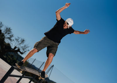 Low angle view of man jumping against clear blue sky