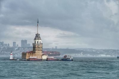 Buildings in sea against cloudy sky