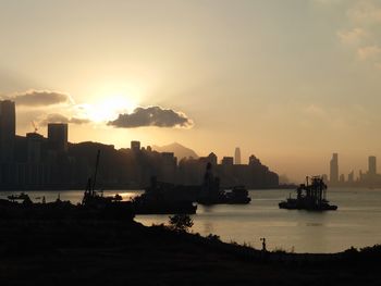 Silhouette buildings by sea against sky during sunset