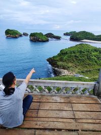 Rear view of woman sitting by sea against sky