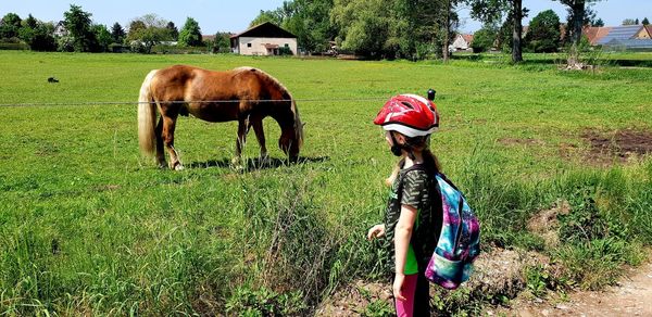 Girl looking at grazing horse on field