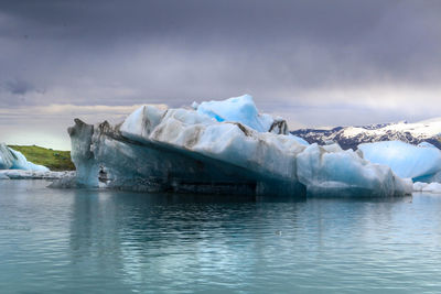 Icebergs floating on sea against cloudy sky