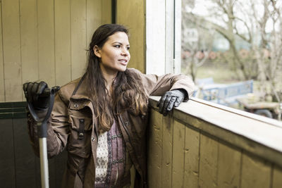 Young woman with pitchfork looking through window of horse stable