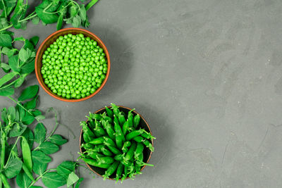 Two bowls of fresh young green peas with seams and peeled leaves against the background of shoots.