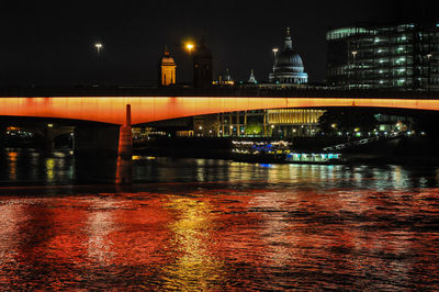 Illuminated bridge over river in city at night