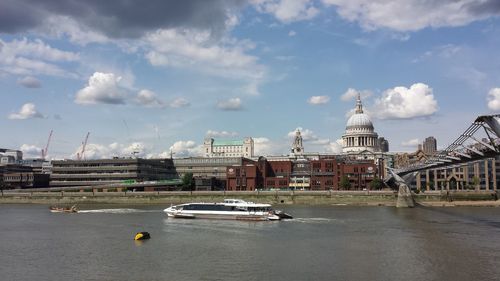 Boats in river by cityscape against sky