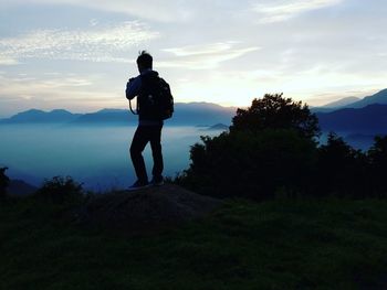 Rear view of hiker photographing fog from mountain peak against sky during sunset