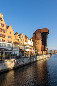 Buildings by river against clear sky in city