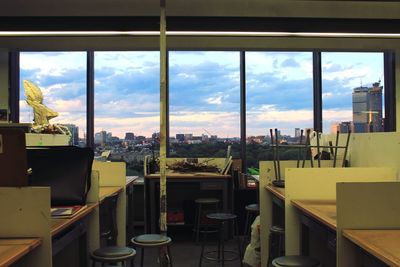 Empty chairs and tables against sky seen through glass window