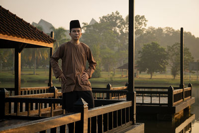 Portrait of man standing on railing against trees