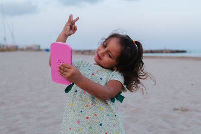 Girl on the beach playing with pink smartphone