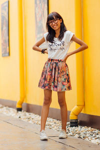 Portrait of young woman standing against yellow wall