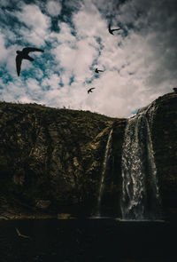 Bird flying over rock formation against sky