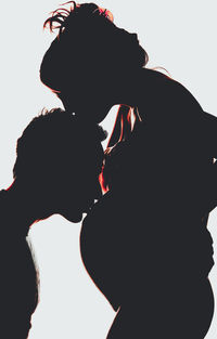 Silhouette man kissing on belly of pregnant woman against white background