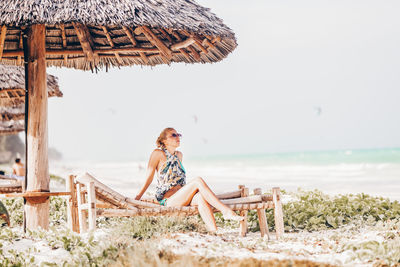 Rear view of woman sitting on beach against sky