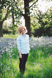 Smiling young woman standing amidst plants at forest