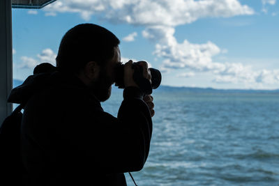 Man looking through binoculars from boat at sea