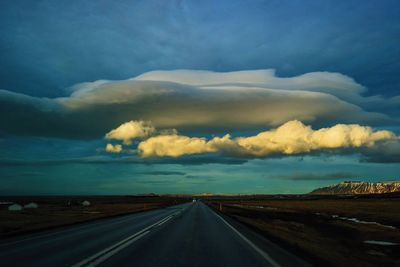 Street amidst field against cloudy sky