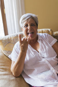 Mature woman making horn sign sitting at home