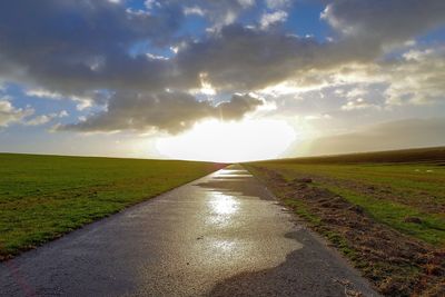 Empty road amidst field against sky